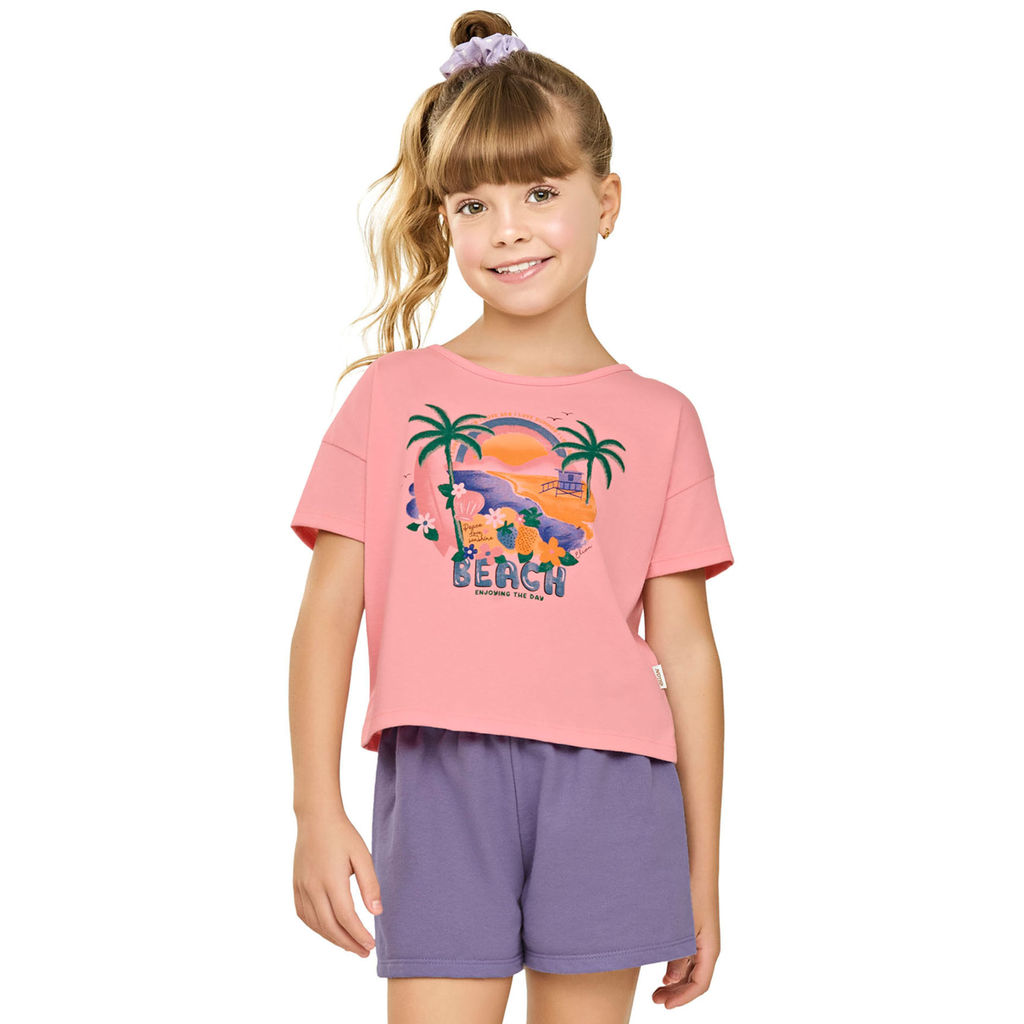 Conjunto Infantil Menina Ombro Deslocado Rosa 1 Menina sorridente vestindo um conjunto infantil rosa de ombro deslocado. A parte superior é uma blusa de manga curta com detalhe de ombro vazado, e a parte inferior é um short combinando, ambos na cor rosa vibrante. A criança está em um ambiente externo, transmitindo conforto e estilo moderno.